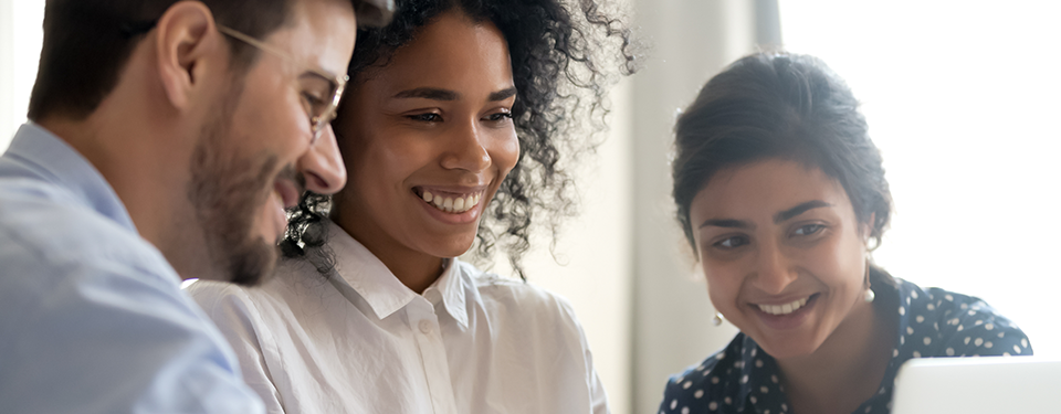 Three multi ethnic colleagues involved in learning new corporate business application seated together in coworking desk, teamwork mentoring concept. Horizontal photo banner for website header design